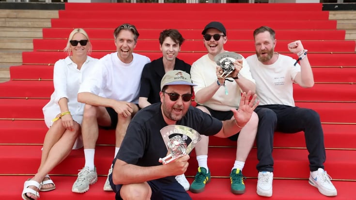 Six people celebrating with trophies on red Cannes Film Festival steps, smiling and posing together.