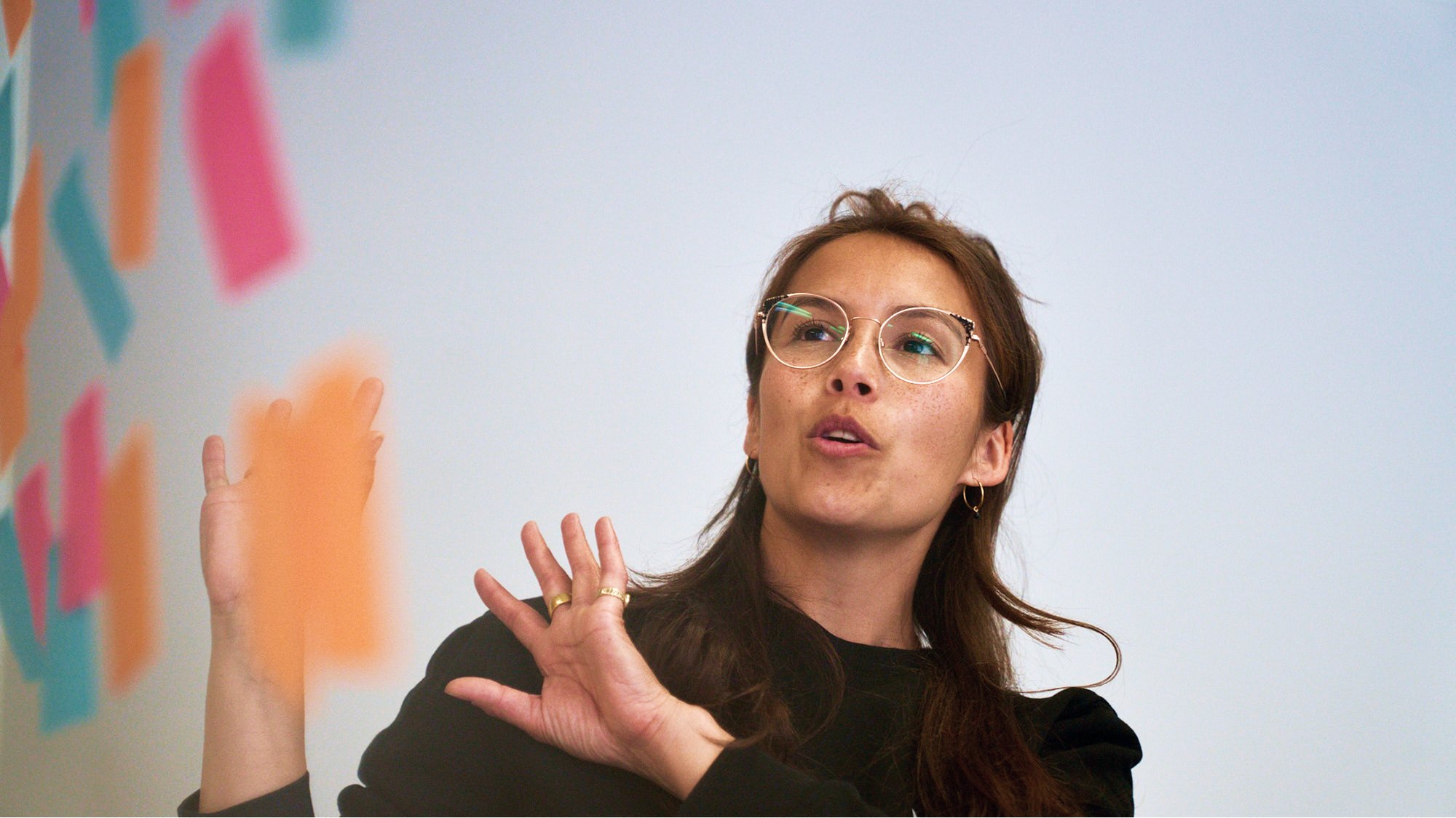 Woman gesturing while presenting in front of colorful sticky notes