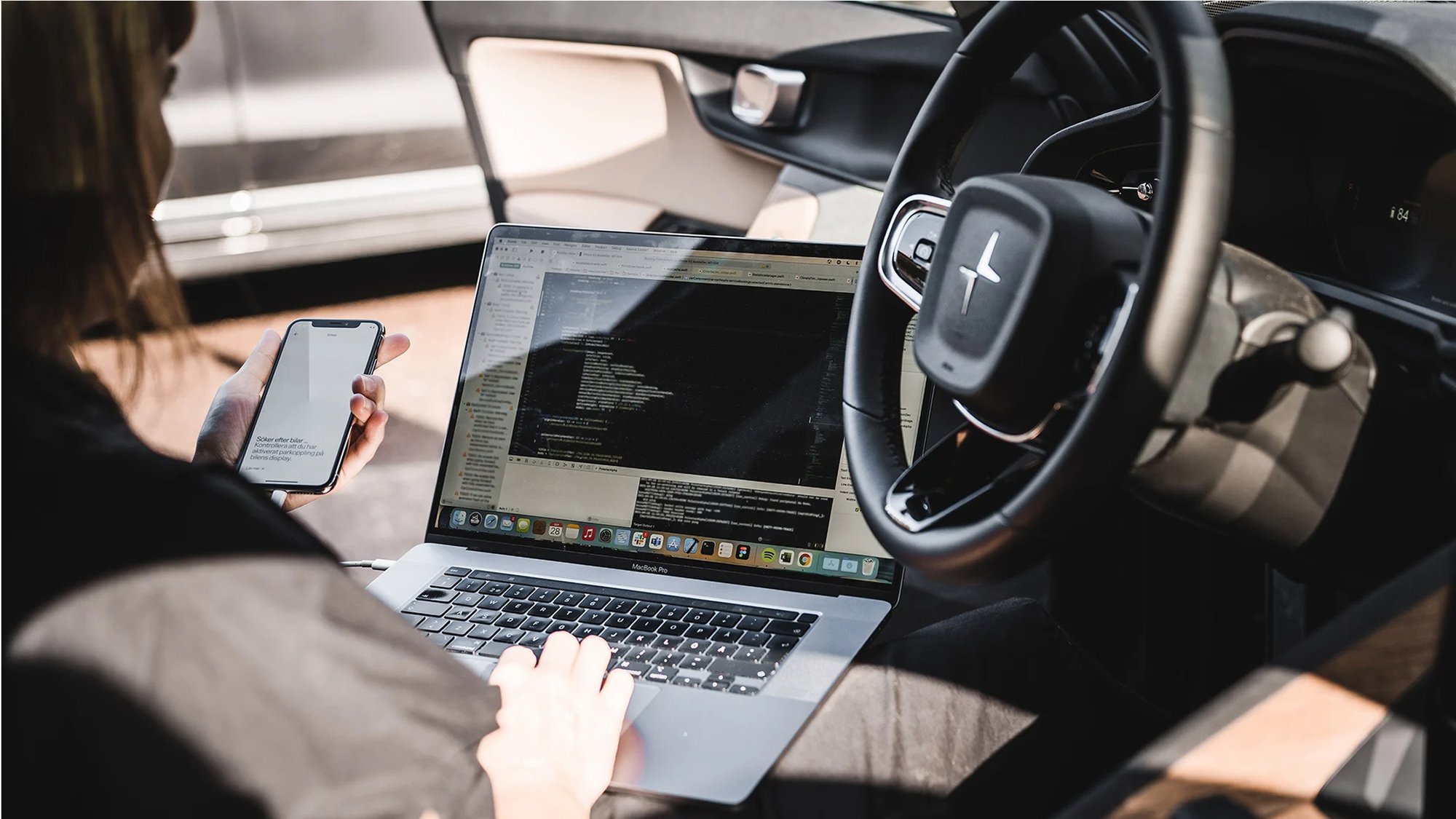 Developer testing app on laptop and phone, inside car.