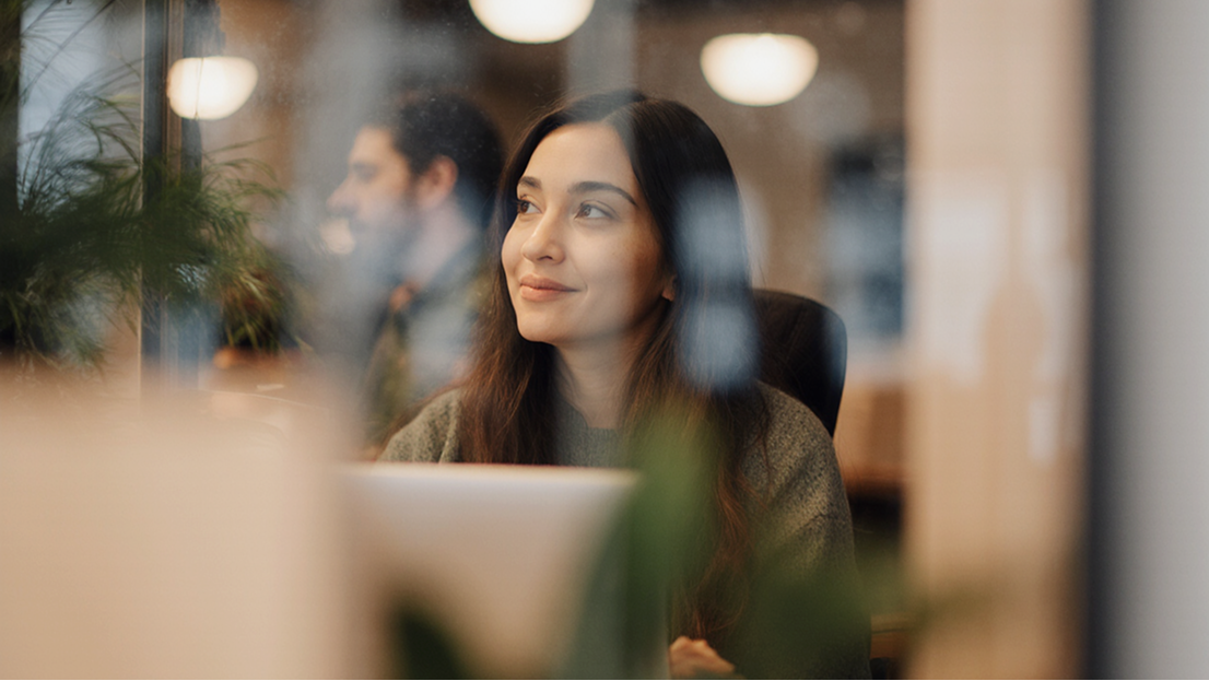 Woman in olive sweater smiling while working on laptop in modern office with warm lighting Woman in olive sweater smiling while working on laptop in modern office with warm lighting