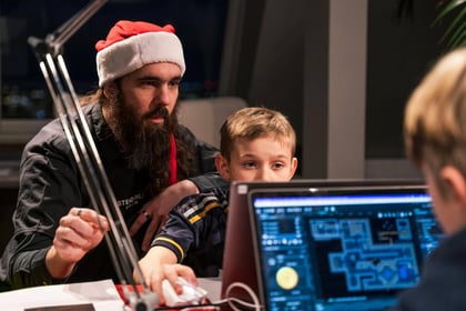 An adult in a santa hat teaching a child to code in front of a computer.