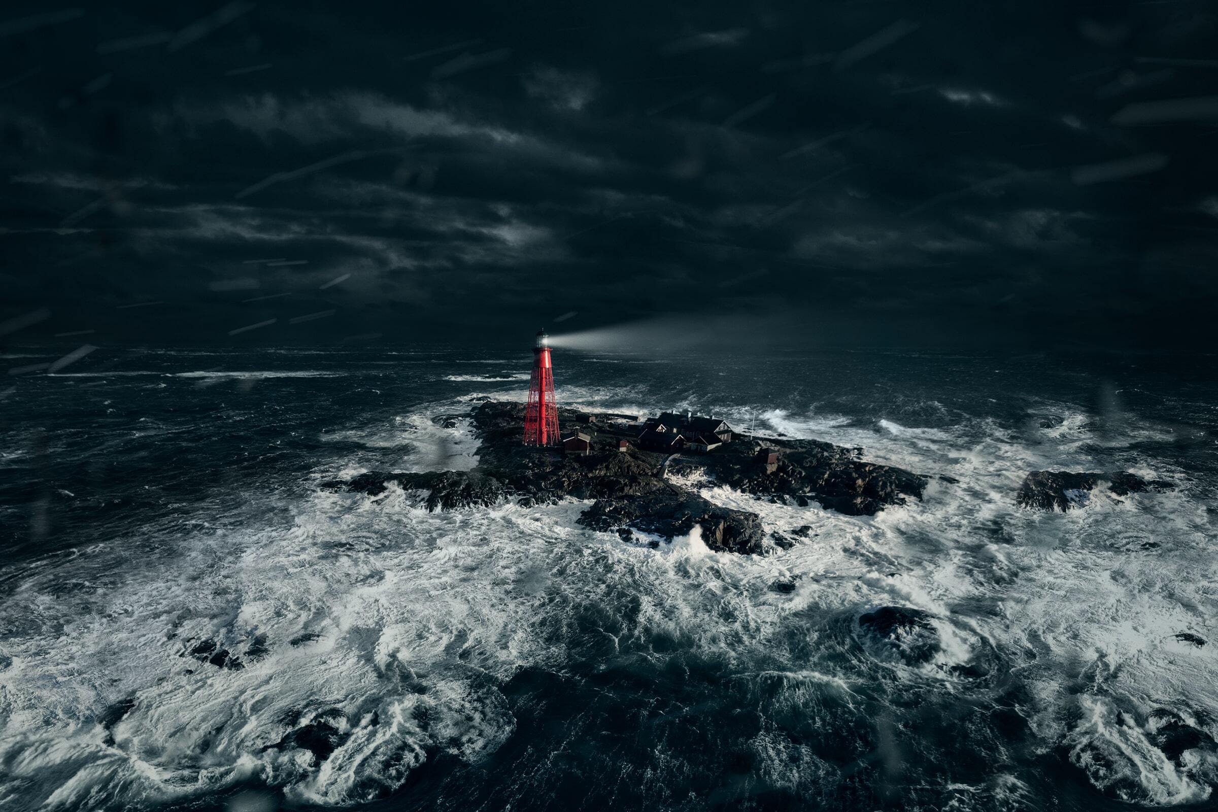 Red lighthouse on rocky island amid stormy sea, waves crashing, under dark, cloudy sky.