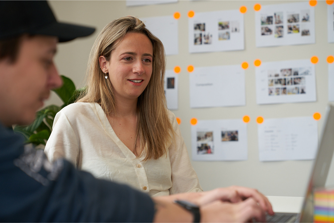 Team member discussing project with colleagues near planning wall with photos