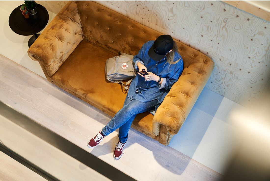 Person using phone while relaxing on velvet sofa in office lounge area