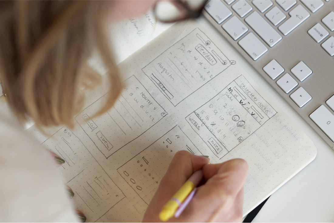 Designer sketching website wireframes in notebook next to keyboard