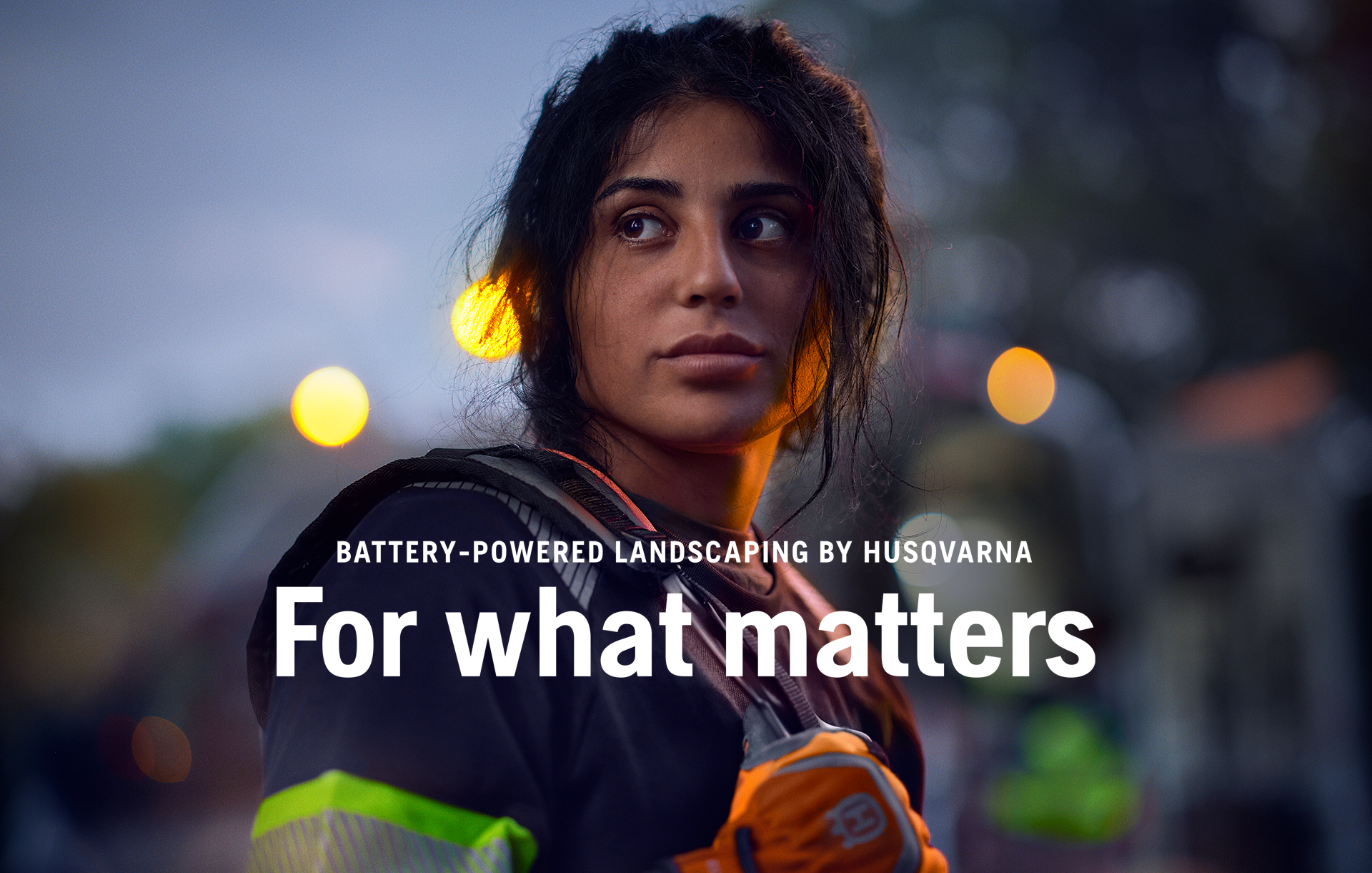 Husqvarna advertisement featuring a person with dark hair in work gear against a dusky background with bokeh lights. Text overlay reads 