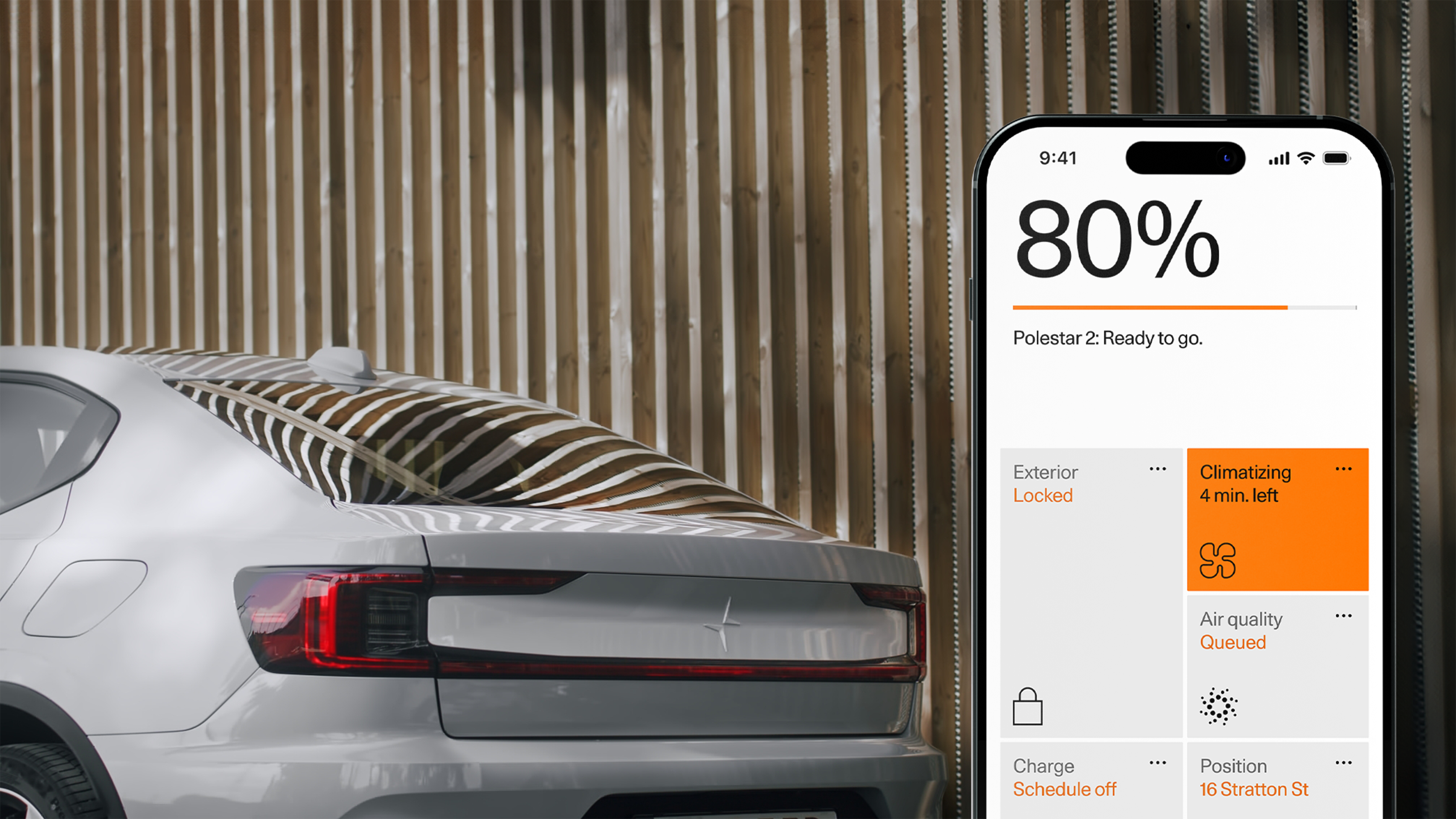 The image shows the rear of a silver Polestar car partially covered with a striped car cover, parked against a wooden slat wall. A smartphone displays the Polestar app, indicating an 80% charge, 