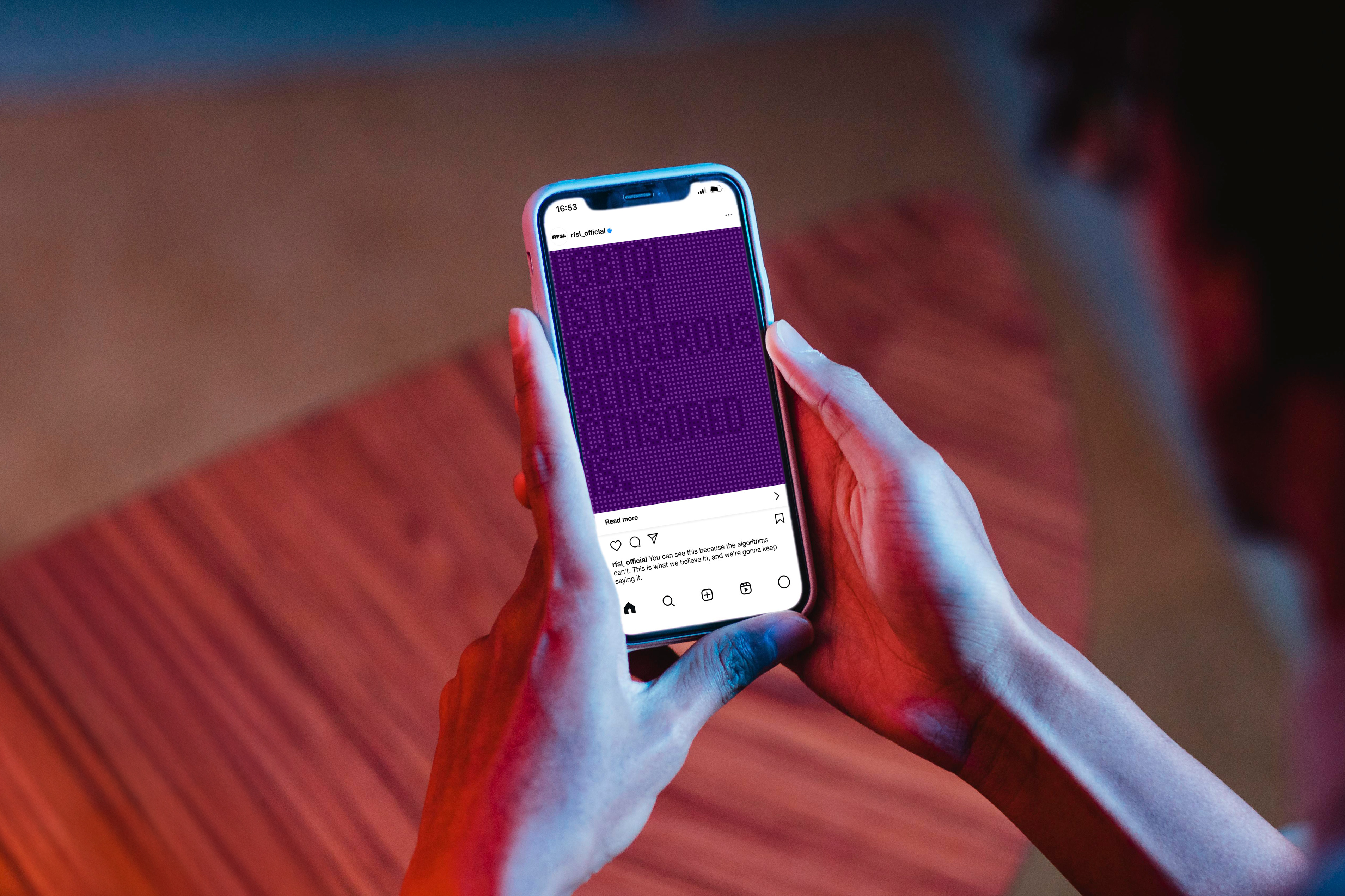 Hands holding phone with social media post under dramatic red and blue lighting