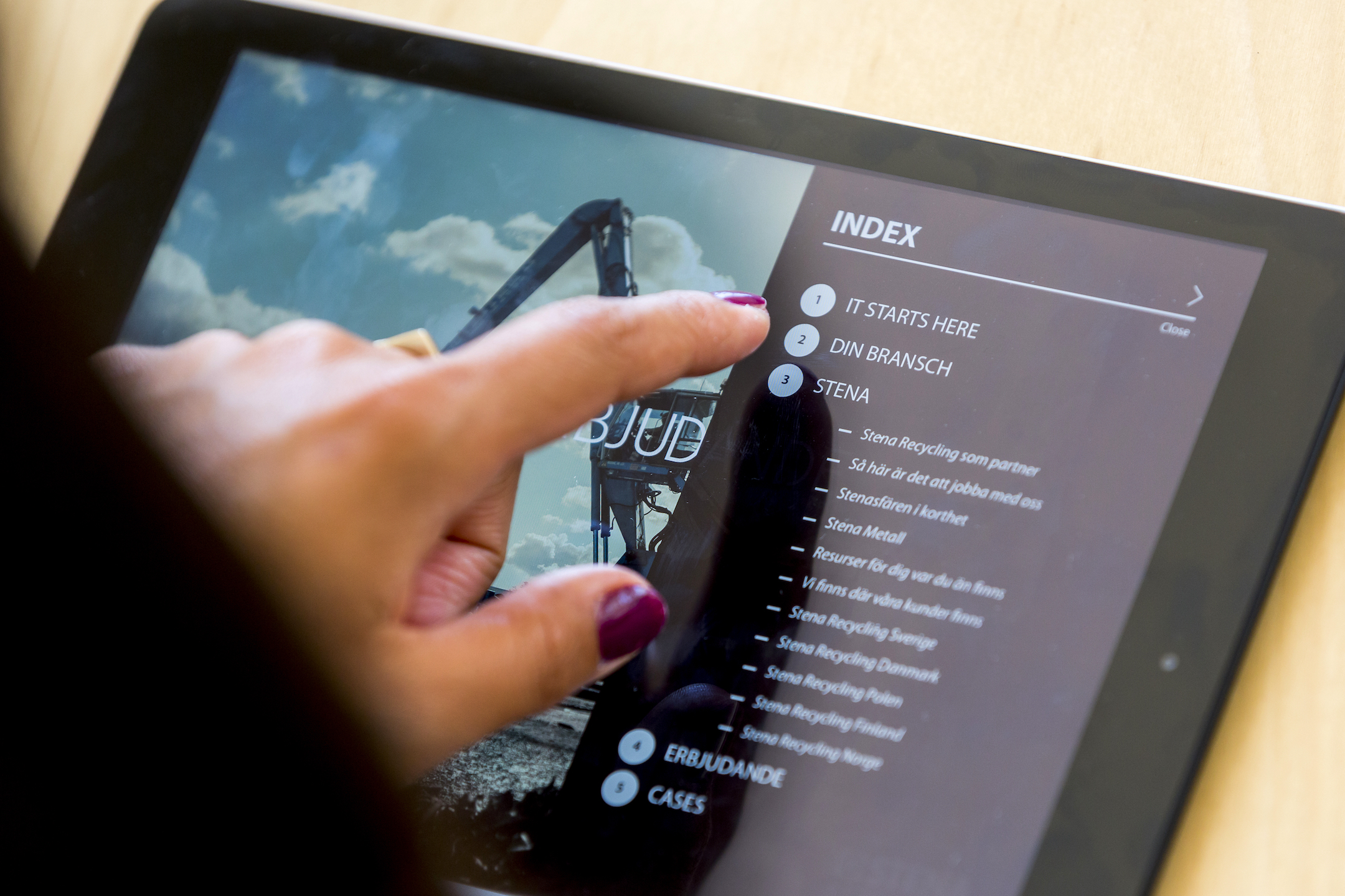 Finger tapping a tablet screen displaying an index page with sections titled 'It Starts Here,' 'Din Bransch,' and 'Stena.'