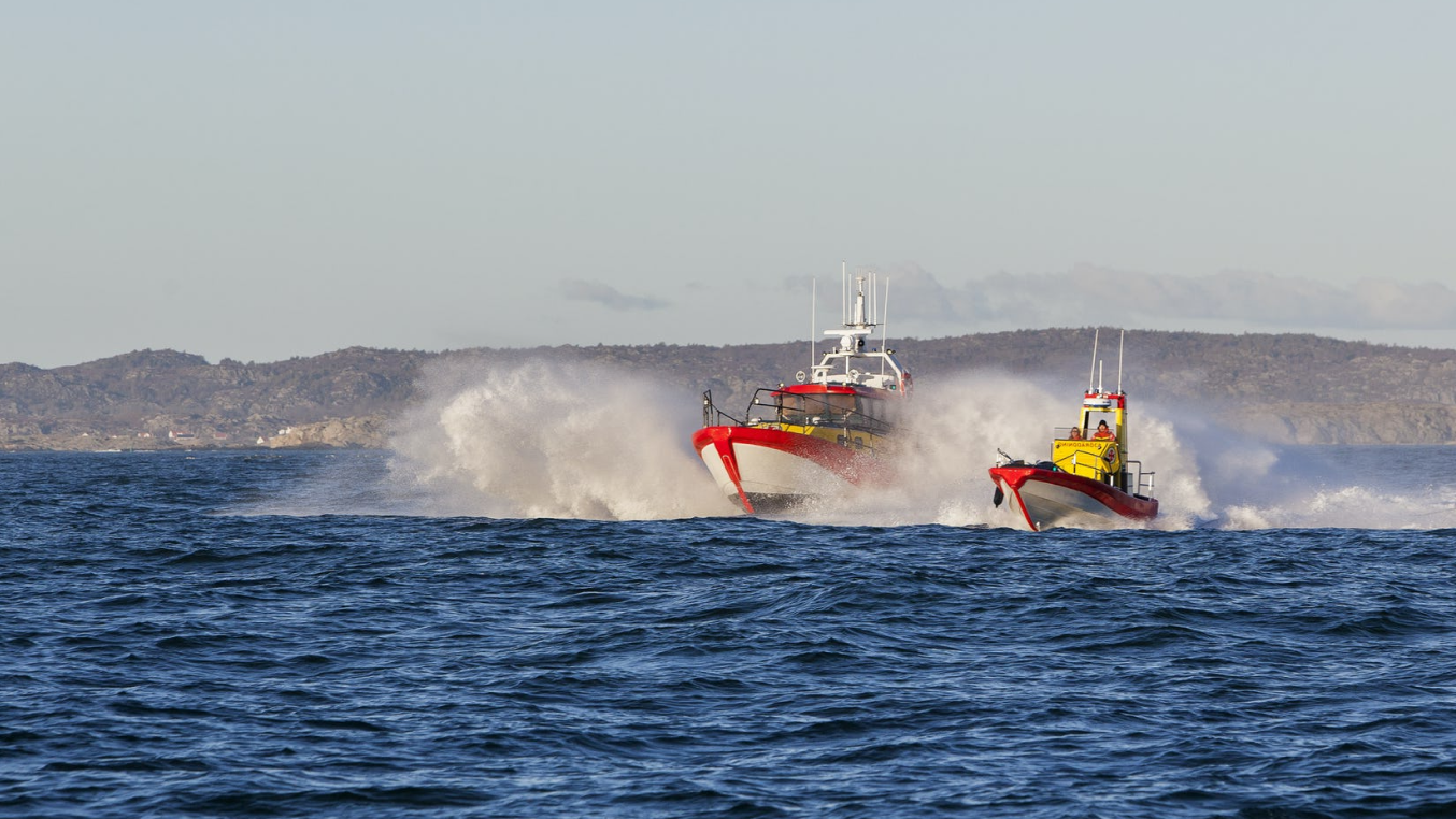 Two rescue boats speeding on choppy water, creating large splashes against a backdrop of distant hills.