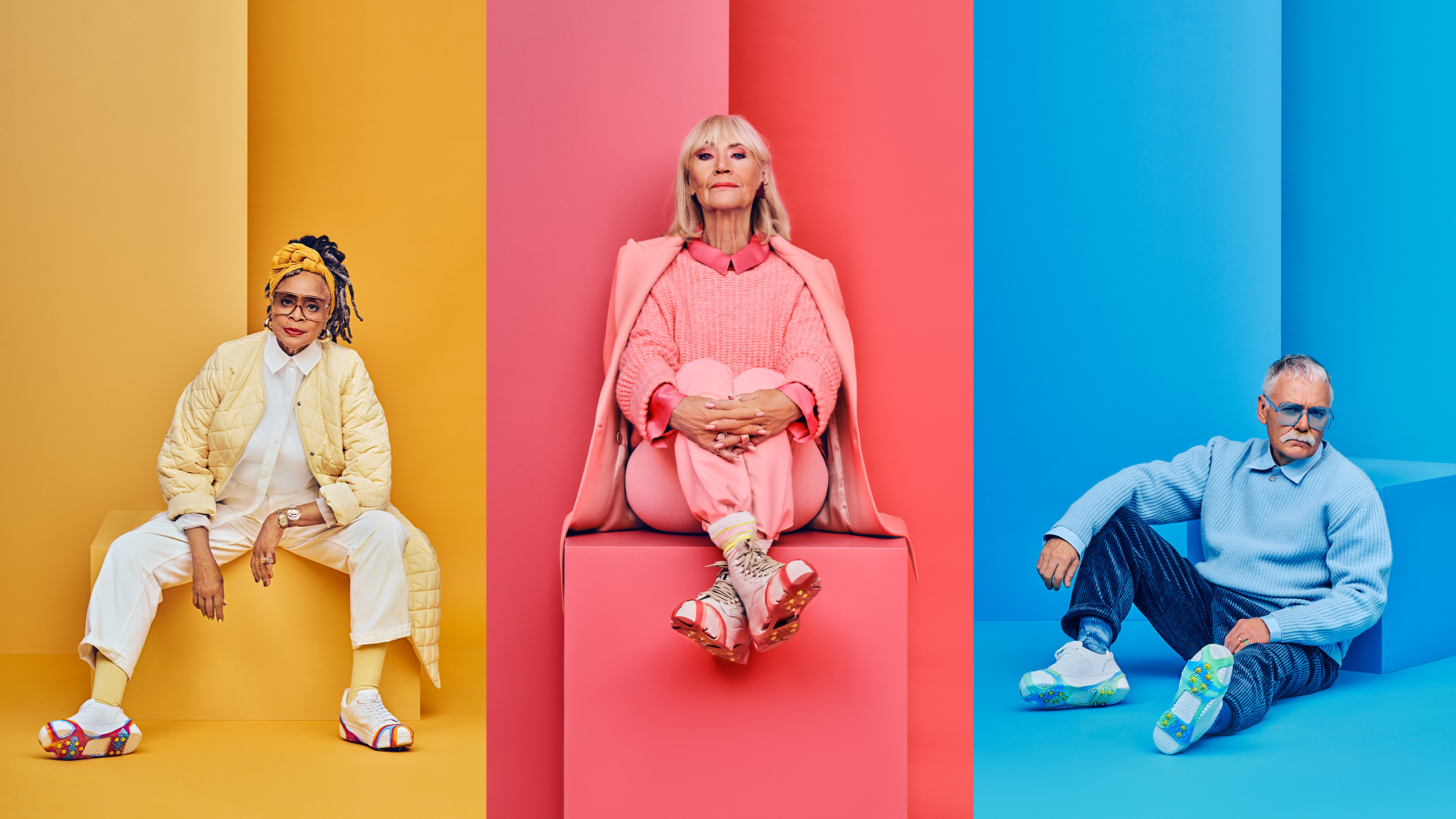 Three individuals wearing vibrant outfits: yellow quilted jacket, pink sweater with matching jacket, and blue sweater with dark trousers.