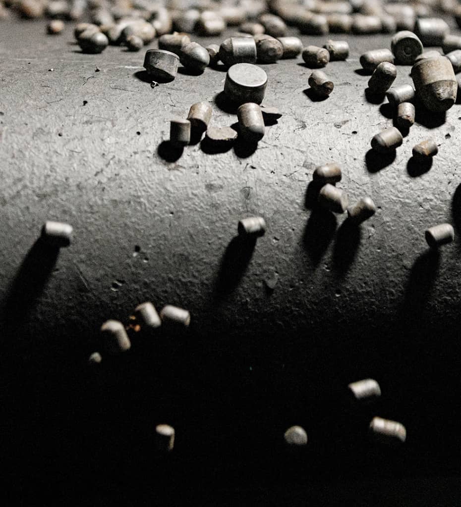 Tiny metal pellets scattered across a textured surface, casting small shadows.
