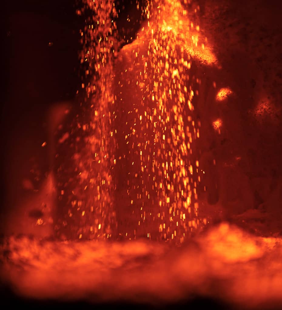 Molten metal pouring with bright orange sparks and intense heat, creating a glowing, fiery scene.