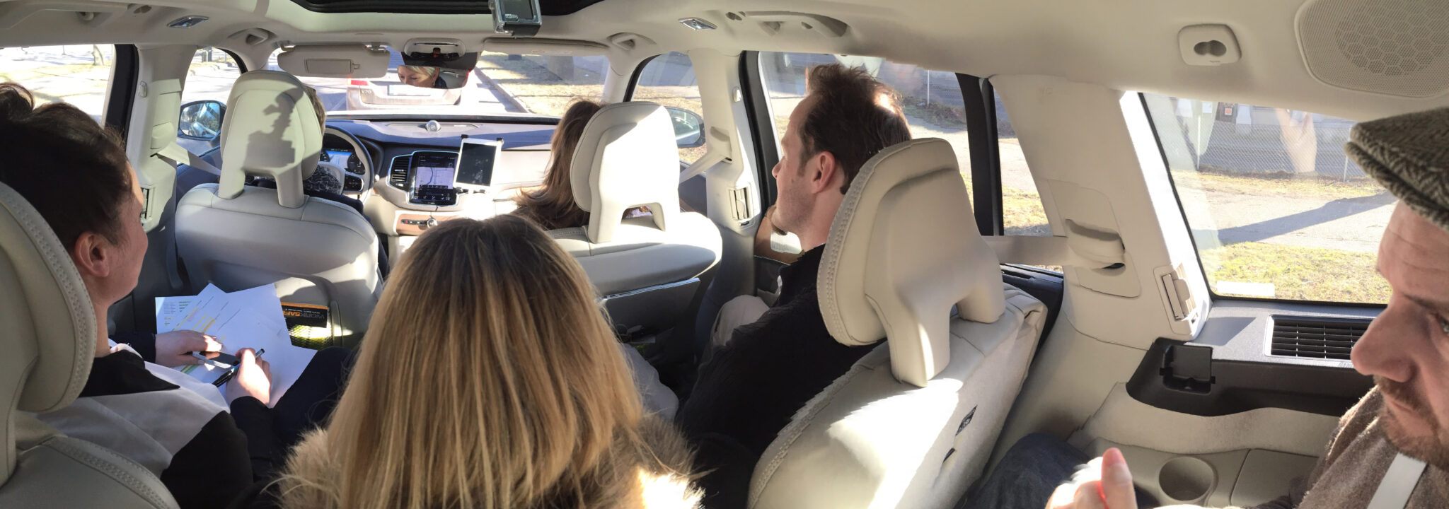 Five people seated in a van, one using a touchscreen in the front and another reviewing documents in the back.